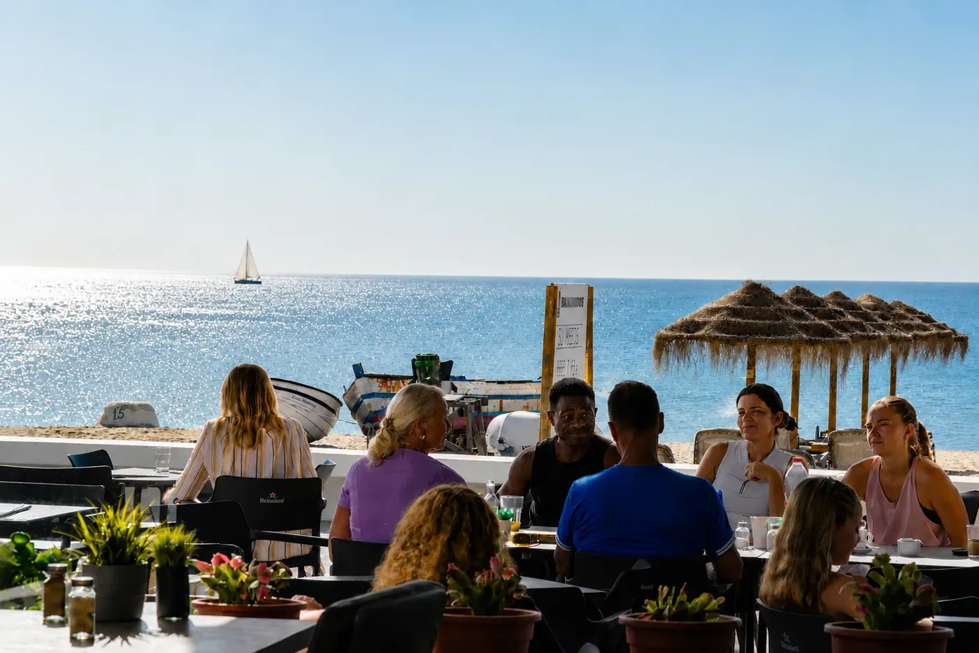 The Bandidos beachfront terrace in Sabinillas — guests at tables with the sea, a sailboat and a thatched parasol beyond